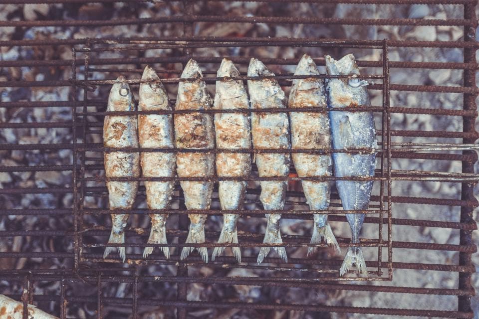 Whole sardines blistering on a grill over embers