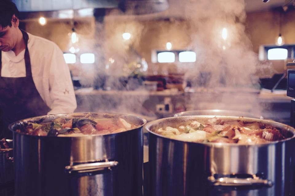 A cook beside steaming pots in a busy restaurant kitchen
