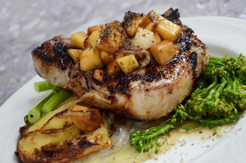 A thick pork chop with roast apple, potatoes and broccolini