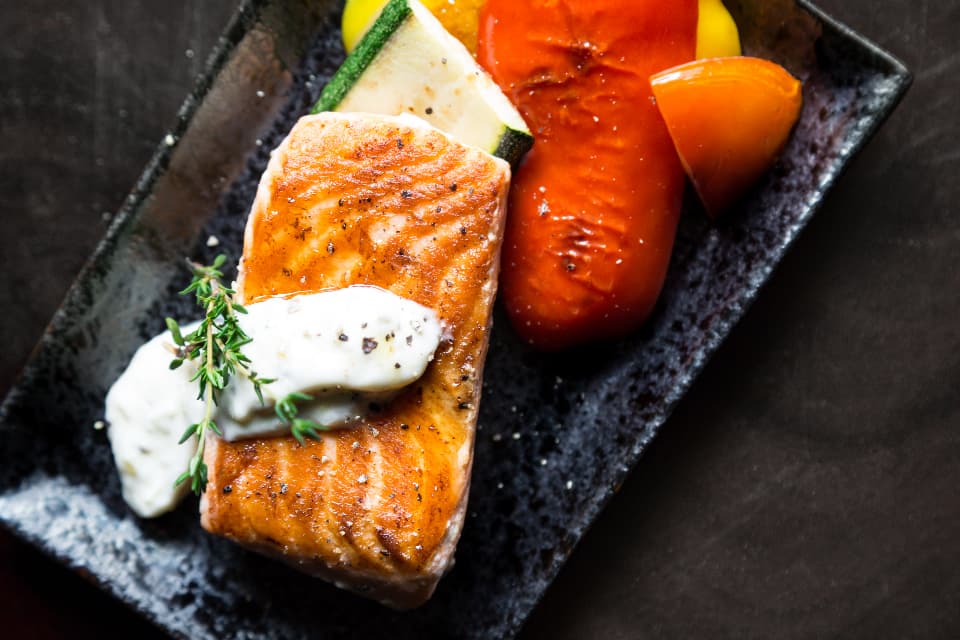 A salmon fillet with herbed yoghurt and roast peppers on a dark plate